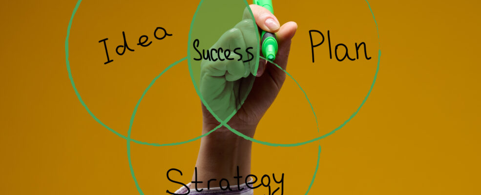 Someone drawing on clear glass a Venn diagram with the words Idea, Plan and Strategy culminating in Success