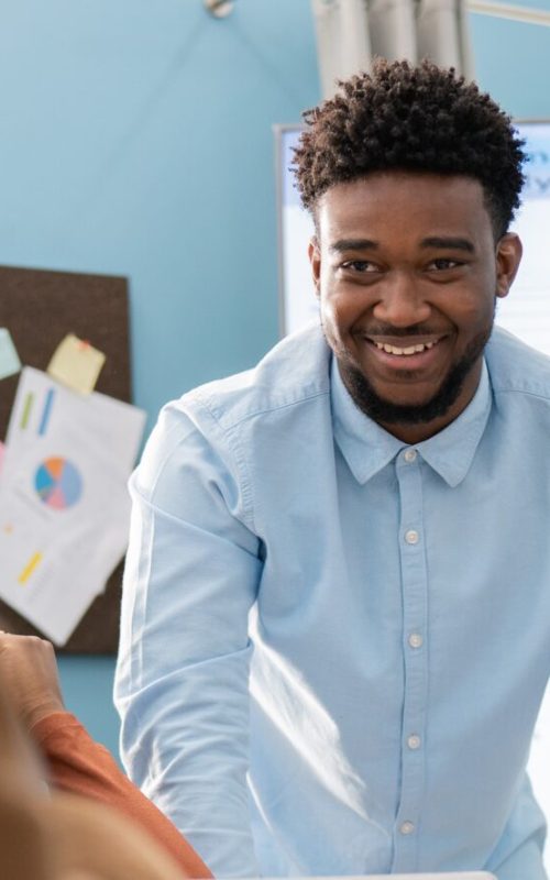 A portrait of a sales representative leaning against a table, framed by two coworkers discussing the presentation he just gave